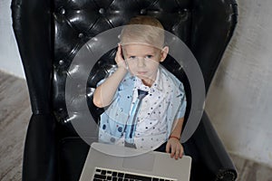 Young businessman using a laptop. funny child in glasses. Fashion portrait of little handsome boy in office