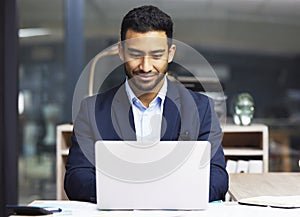 Young businessman using a laptop, trading on the stock market. Smiling trader working online with a computer and going