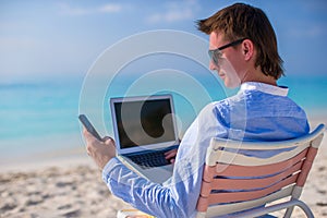 Young businessman using laptop on tropical beach