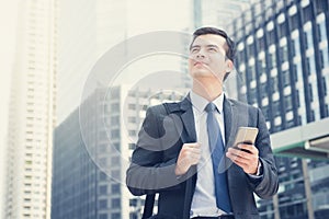 Young businessman using mobile phone while carrying bag in the city