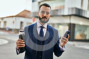 Young businessman using smartphone and holding bottle of water at the city