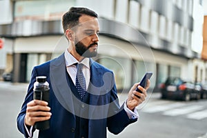 Young businessman using smartphone and holding bottle of water at the city