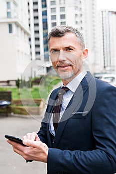 Young businessman using smartphone in the urban environment. The man in suit full length photo