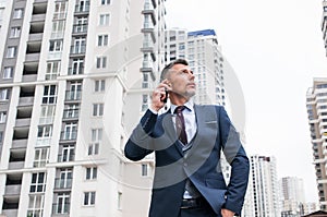 Young businessman using smartphone in the urban environment. The man in suit full length photo