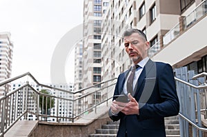 Young businessman using smartphone in the urban environment. The man in suit full length photo