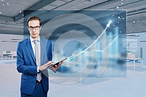 Young businessman using tablet with abstract growing business chart hologram on blurry office interior background. Trade, finance