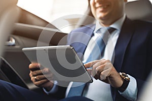 Young businessman using tablet pc while sitting on back seat of a car. Caucasian male business executive by a taxi and