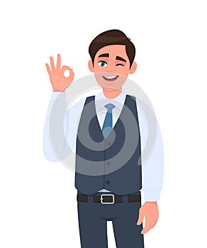 Young businessman in waistcoat showing okay or OK gesture and winking eye. Person making symbol of good or cool sign.