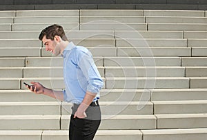 Young businessman walking outdoors and looking at mobile phone