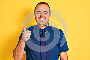 Young businessman wearing denim casual shirt and tie over isolated yellow background doing happy thumbs up gesture with hand