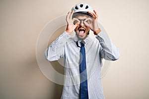 Young businessman wearing glasses and bike helmet standing over isolated white bakground doing ok gesture like binoculars sticking