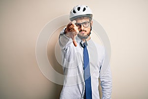 Young businessman wearing glasses and bike helmet standing over isolated white bakground looking unhappy and angry showing