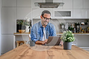 Young businessman wearing glasses laughing and working over laptop on desk in home office