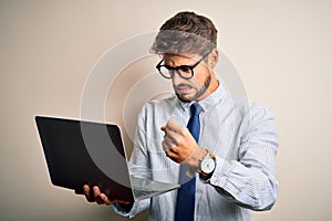 Young businessman wearing glasses working using laptop standing over white background annoyed and frustrated shouting with anger,