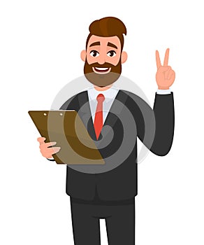 Young businessman wearing a suit holding clipboard and making or showing victory, V, peace, two gesture with hand finger. Person