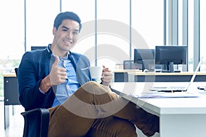 A young businessman wearing a suit and a long sleeve shirt inside and sitting smart poses has a feel happy smile in a modern