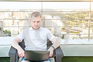 Young businessman working on Computer laptop comfortably sitting on chair on the office terrace balcony with Urban Landscape on Ba