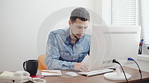 Young businessman working on computer in stylish modern office. Computer, phone and cup on the table. Shot in 4k