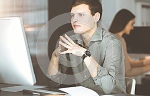 Young businessman working on his computer sitting at the desk in office. Headshot portrait of a man