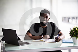 Young businessman working on his laptop in office. Young african executive sitting at his desk surfing internet on laptop computer