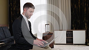 Young businessman working from hotel room on business trip. A man sitting on bed and using laptop