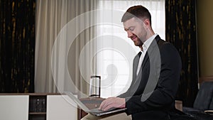Young businessman working from hotel room on business trip. A man sitting on bed and using laptop