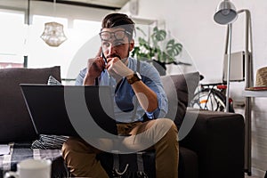 Young businessman working on laptop computer while sitting on sofa at home