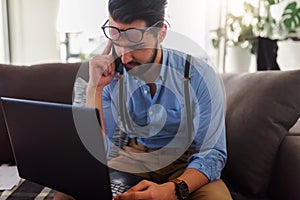 Young businessman working on laptop computer while sitting on sofa at home