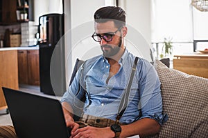 Young businessman working on laptop computer while sitting on sofa at home