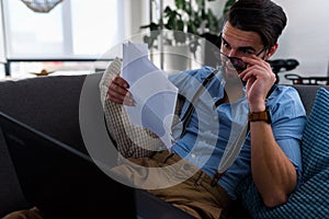 Young businessman working on laptop computer while sitting on sofa at home