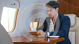 Young businessman working on laptop and drinking coffee in his private plane. Successful business millionere man