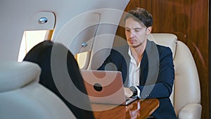Young businessman working on laptop in his private plane. Successful business millionere man traveling in first class