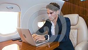 Young businessman working on laptop in his private plane. Successful business millionere man traveling in first class