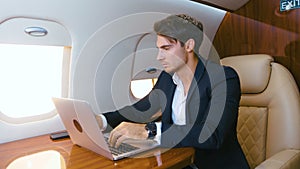 Young businessman working on laptop in his private plane. Successful business millionere man traveling in first class