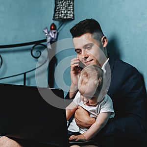 Young businessman working at laptop from home and watching baby