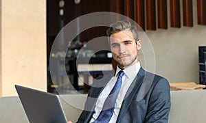 Young businessman working on laptop, sitting in hotel lobby waiting for someone.