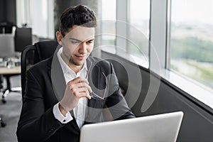 Young businessman working at office. Handsome professional man using laptop computer. Management, internet marketing, finance, bus