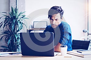 Young businessman working at sunny office on laptop while sitting at the wooden table.Man analyze document on computer