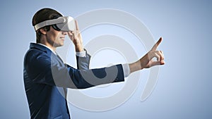 Young businessman working in virtual reality office in VR glasses, presses his finger virtual interface on abstract light blue