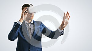 Young businessman working in virtual reality office in VR glasses, presses his hand virtual interface on abstract light grey