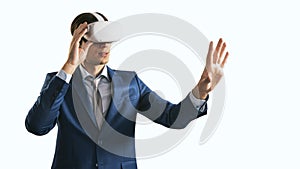 Young businessman working in virtual reality office in VR glasses, presses his hand virtual interface on abstract white backdrop.