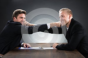 Young Businessmen Fighting At Wooden Desk