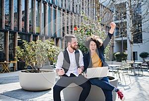 Young businesspeople with laptop outdoors in courtyard, expressing excitement.