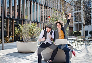 Young businesspeople with laptop outdoors in courtyard, expressing excitement.