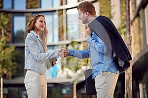 Young businesspeople shaking hands in front of a building