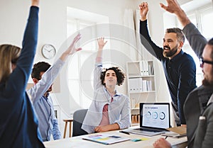 Young businesspeople sitting around table in a modern office, celebrating success.