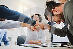 Young businesspeople sitting around table in a modern office, making fist bump.