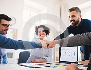 Young businesspeople sitting around table in a modern office, making fist bump.