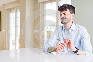 Young businesss man sitting on white table disgusted expression, displeased and fearful doing disgust face because aversion