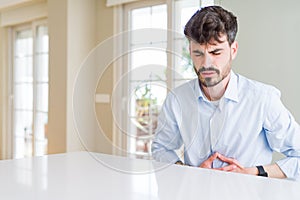 Young businesss man sitting on white table with hand on stomach because indigestion, painful illness feeling unwell